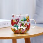 Glass mug with red and green pressed flowers on side table