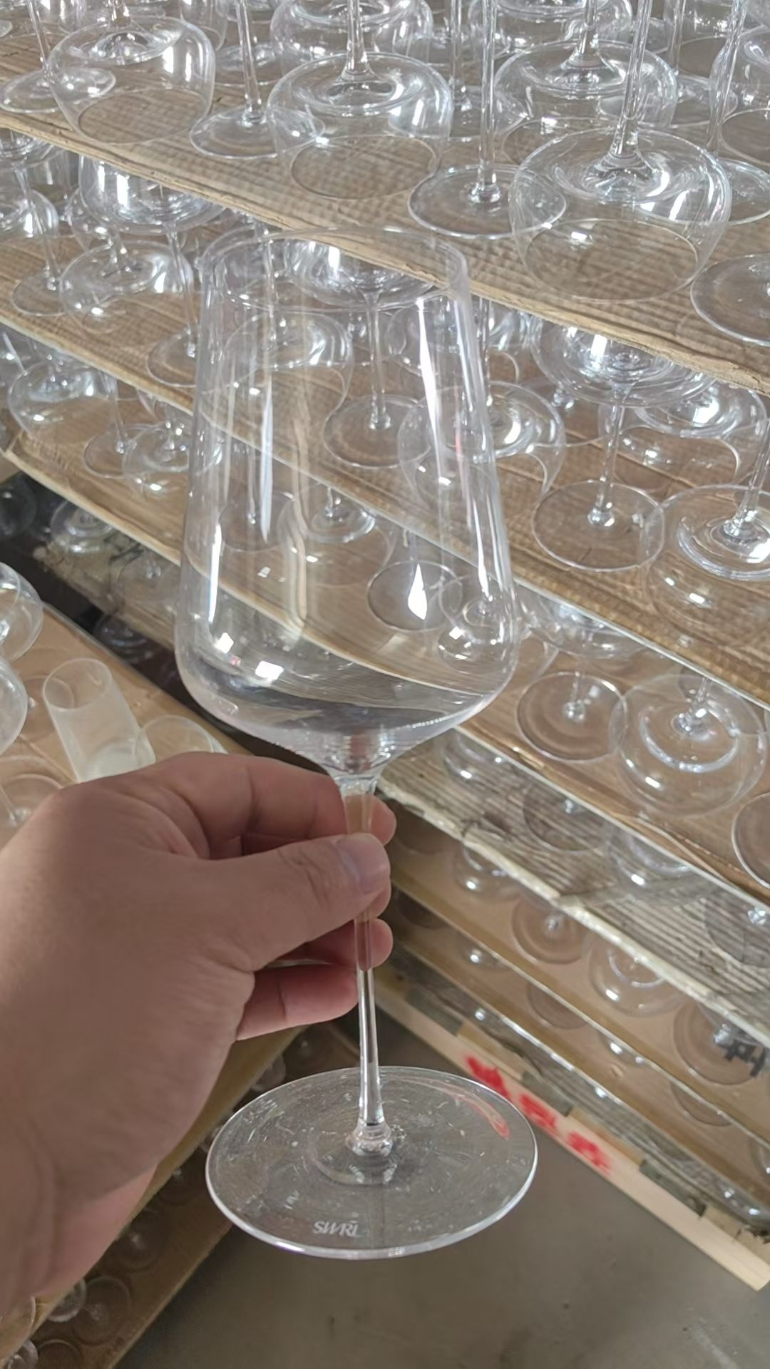 Handmade clear glass red wine goblet held in workshop